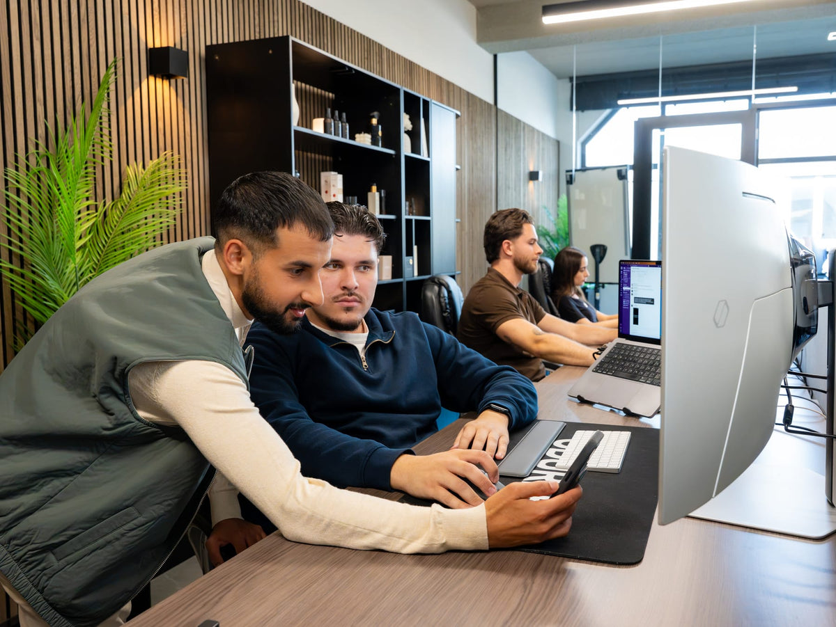 One of the founders shows a colleague something on his phone, with the team in the background.