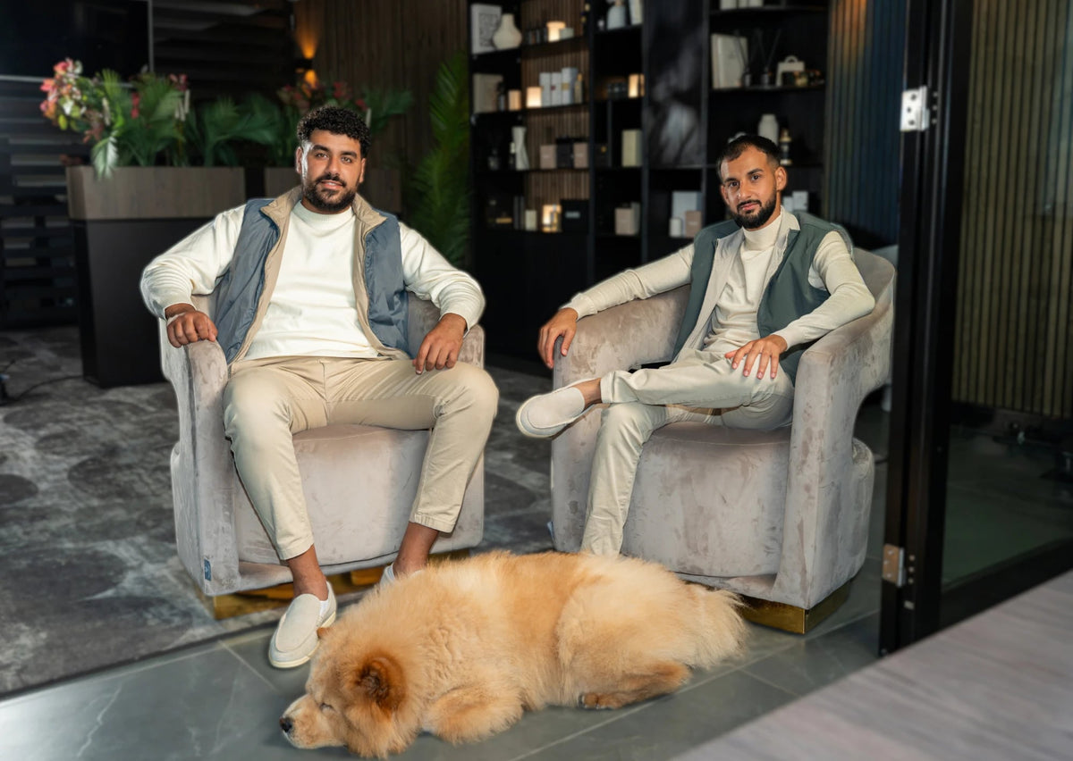 The two founders of Oduree in velvet armchairs in the lounge, with the dog on the floor in front of their chairs.