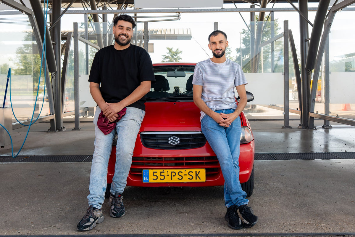 Marco and Kiro sit on the bonnet of a red Suzuki Alto at the car wash.